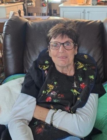 Elderly woman sitting in a chair, smiling gently.