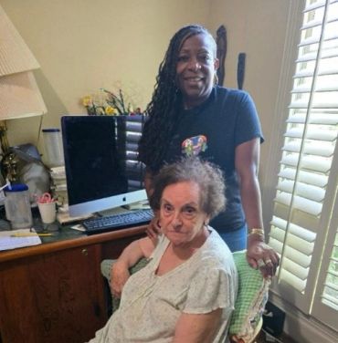 Two women, one seated and one standing in a cozy room.