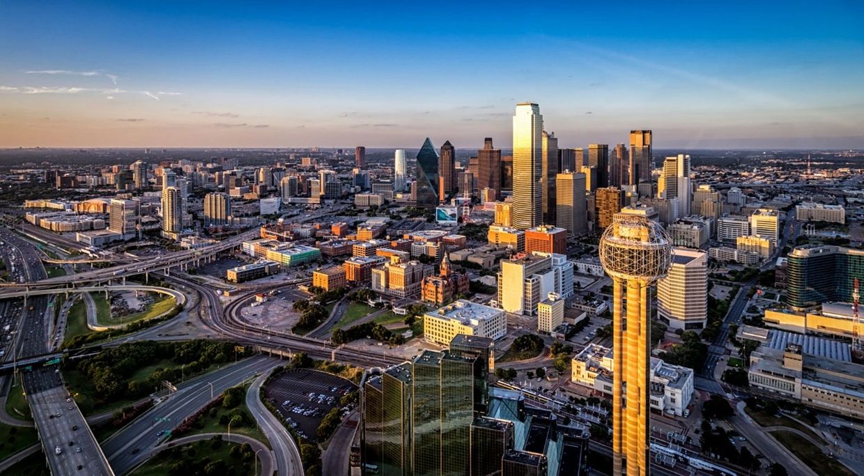 Aerial view of a city skyline with highways and modern buildings at sunset.