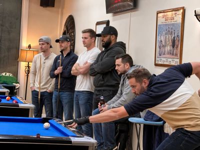 A group of men watching one man take a shot in a pool game.