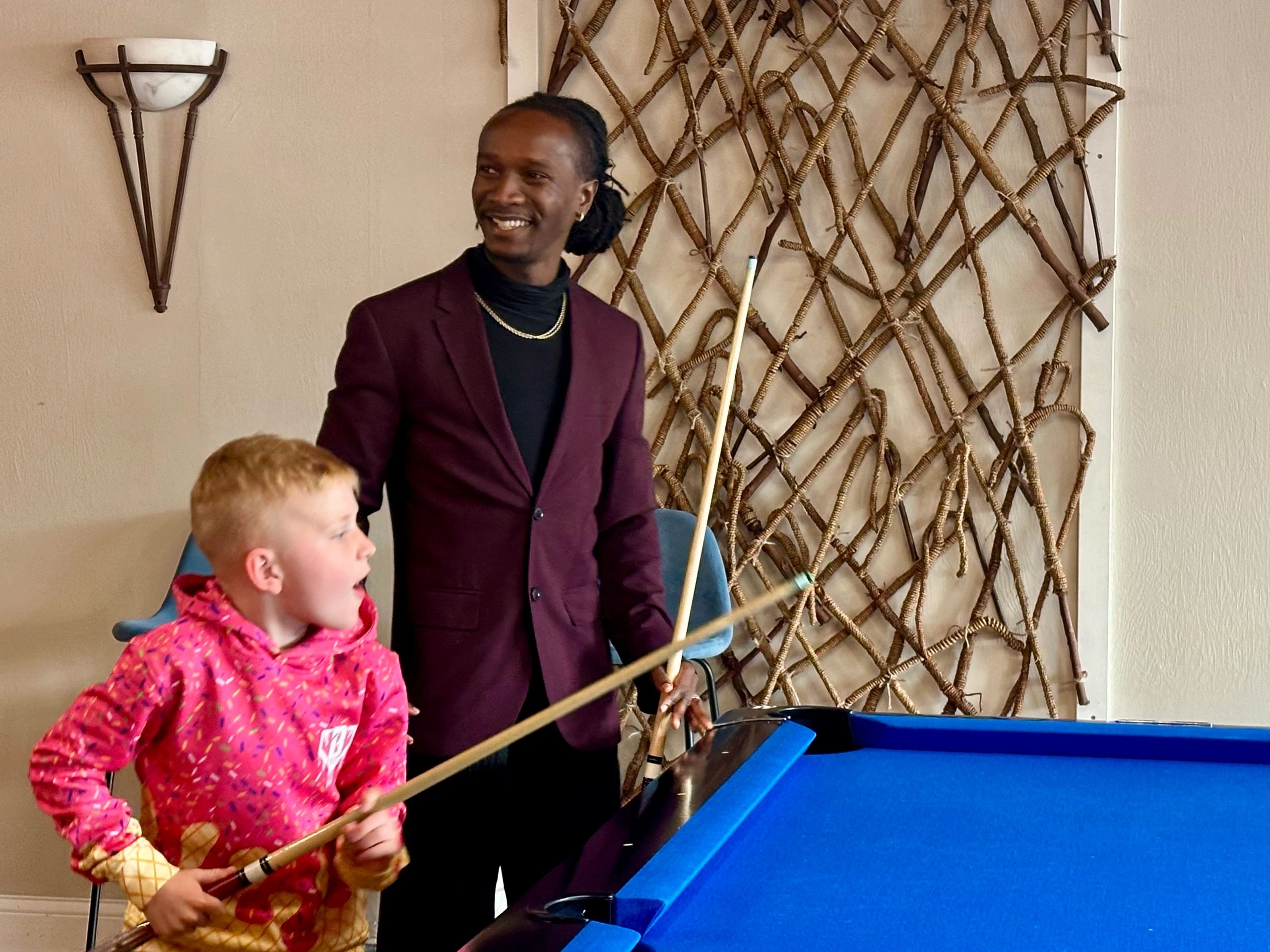 A young boy and a man play pool together indoors, smiling and focused.