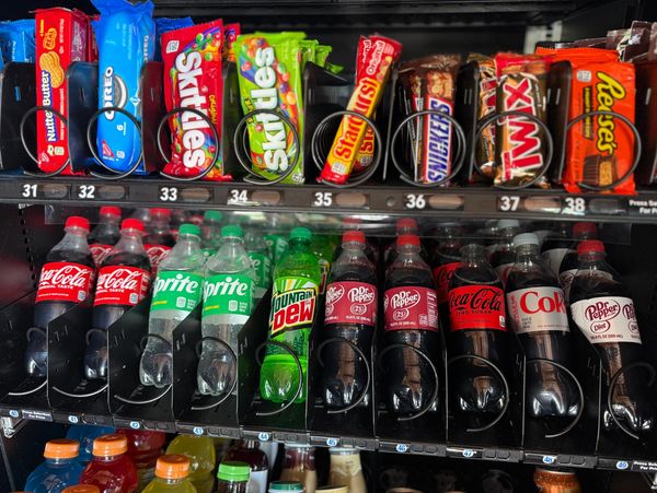A vending machine stocked with candies and soda bottles.
