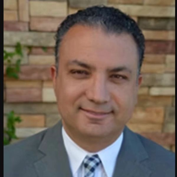 Man in a suit smiling against a brick wall background.