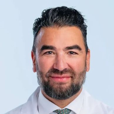 Professional man with beard and white coat smiling.