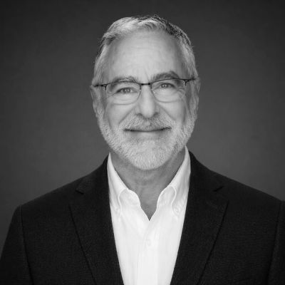Smiling mature man in glasses and suit jacket against a plain background.