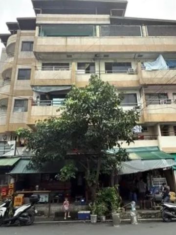 Multi-story building with trees and parked scooters in front.