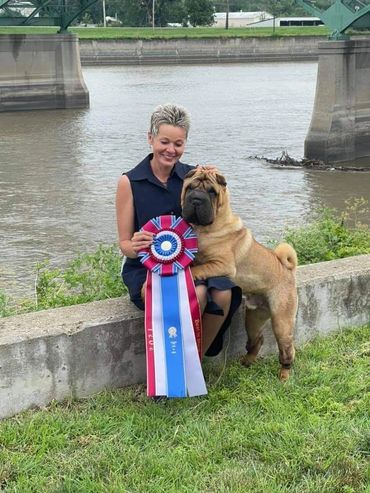 Riverfront view of a woman and her Shar Pei holding their best in show ribbon