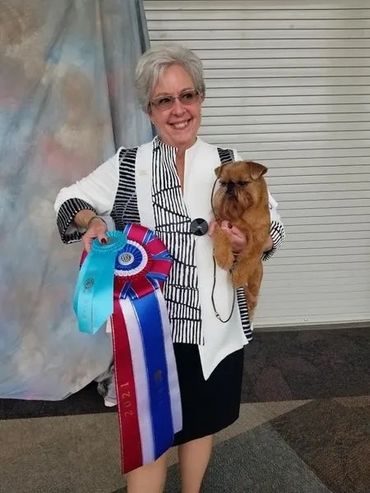 A smiling woman holding her dog and their best in show ribbon