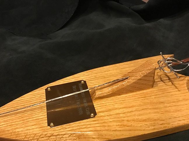 A glass sword display mounted on a wooden base with a metal plaque.