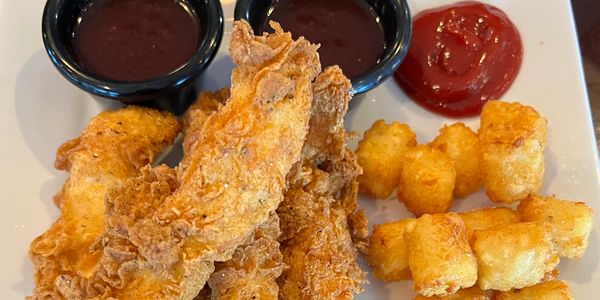 Crispy fried chicken tenders with tater tots and dipping sauces on a white plate.