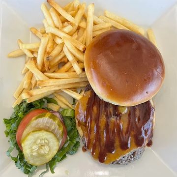 A classic American burger served with a side of fries on a white square plate. 