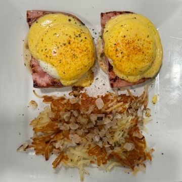 Two English muffin halves grilled and topped with ham, two over-easy eggs and hollandaise sauce. 