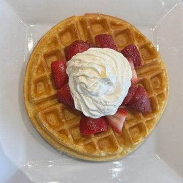 One large homemade light and fluffy waffle topped with strawberries and whipped cream. 
