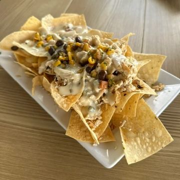 Plate of loaded nachos with cheese, beans, shredded chicken, jalapeños, and corn salsa. 