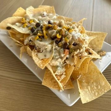 Plate of loaded nachos with cheese, beans, jalapeños, shredded chicken and corn salsa. 