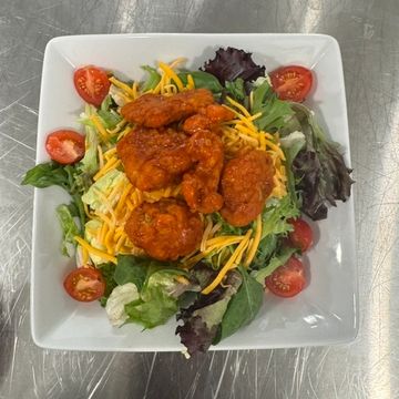 A white square salad bowl filled with lettuce, shredded cheese, tomato and buffalo chicken. 