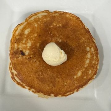 A white plate topped with one golden fluffy pancake served with whipped butter on top. 
