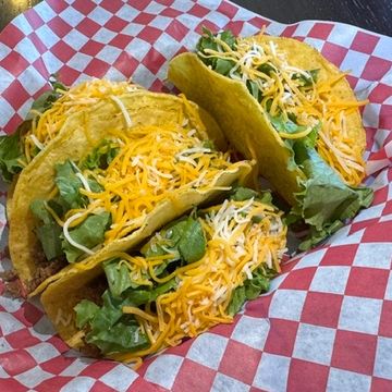 Three hard shell beef tacos with shredded lettuce and cheese sitting on checkered paper. 