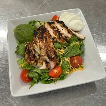 A white square salad bowl filled with lettuce, tomato, grilled chicken, avocado, egg and cheese. 