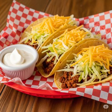 Three corn tortilla shell beef tacos with shredded lettuce and cheese and a side of sour cream. 
