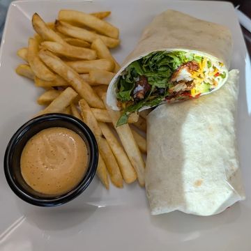 A buffalo chicken wrap and a side of fries and dipping sauce sitting on a white square plate.