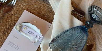 Elegant table setting with a menu, name card on a shell, and blue wine glass.