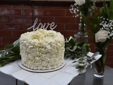 A detail shot of a small wedding cake with flowers around it and a "LOVE" sign on top of the cake