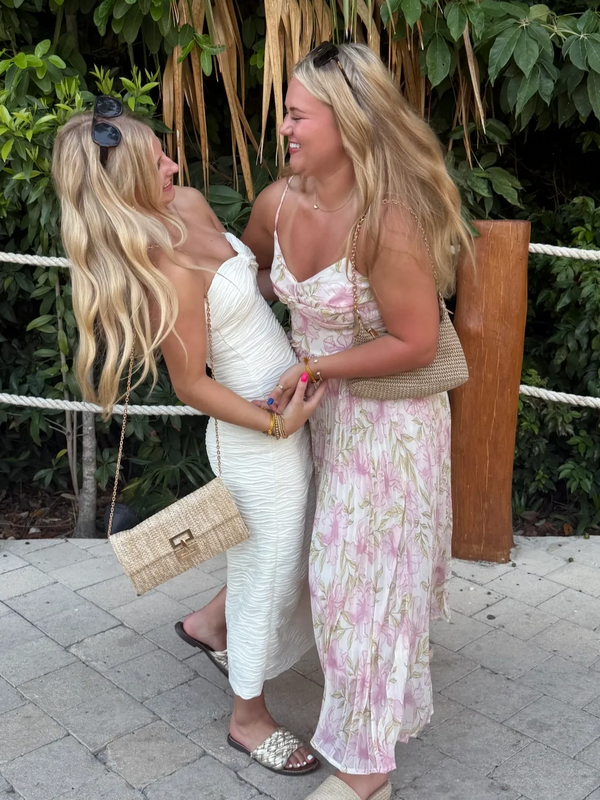 Two women in summer dresses laughing and holding hands outdoors.
