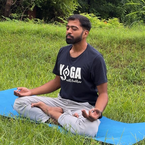 Man meditating in lotus pose on a blue yoga mat in a lush green garden.