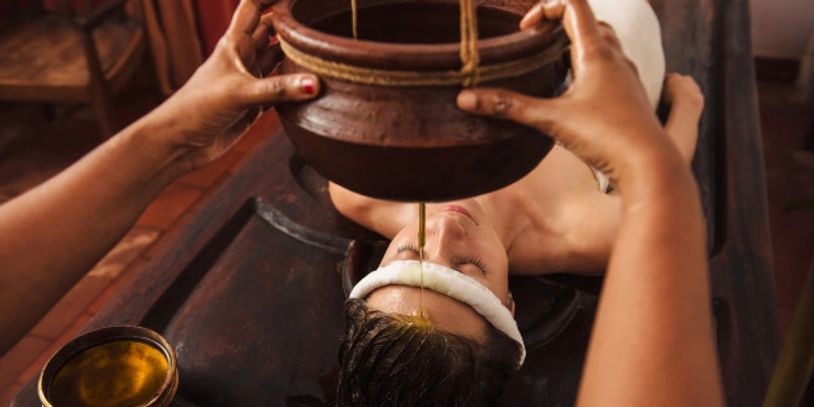 Person receiving Ayurvedic oil treatment with oil dripping on forehead.