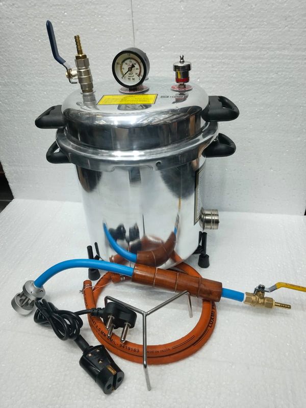 A stainless steel pressure cooker with attached hoses and electrical plugs.