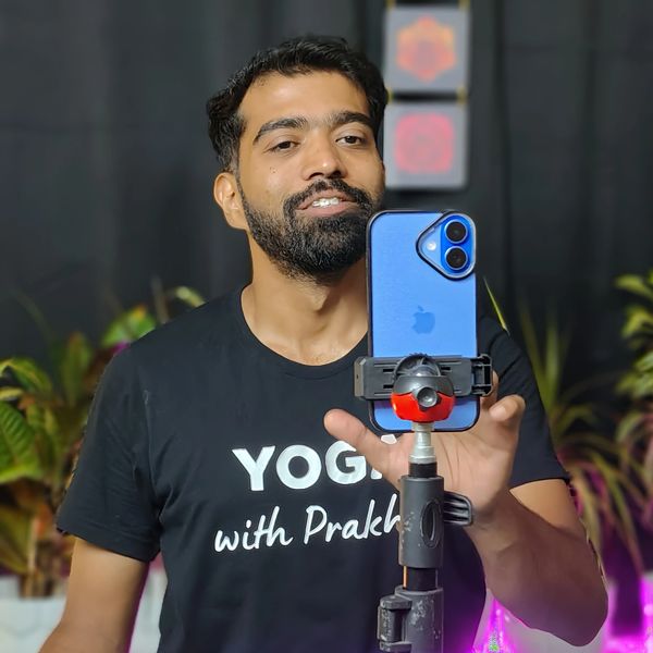 Man practicing yoga and recording with a smartphone on a tripod.