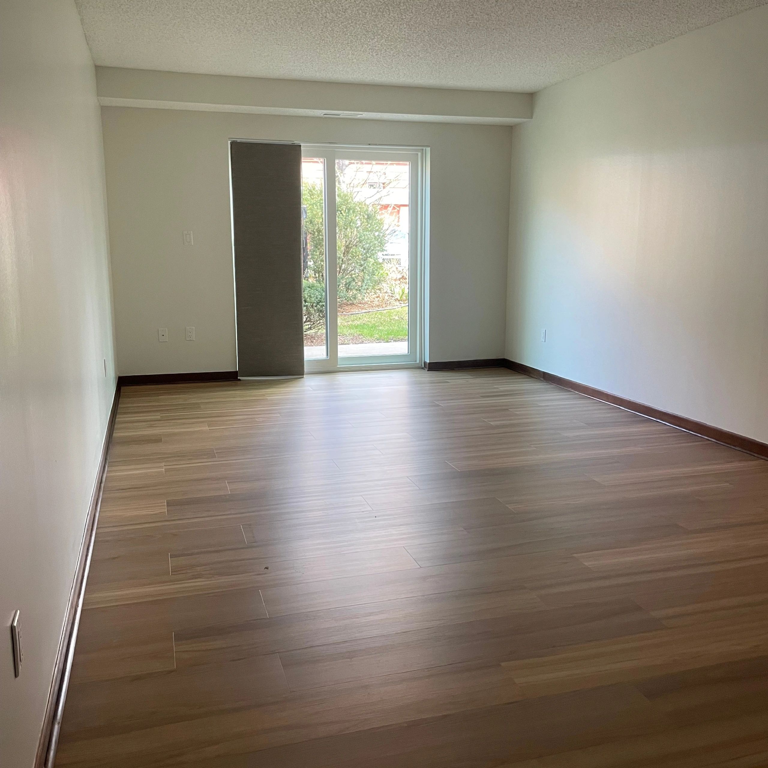 Empty room with wooden flooring and sliding glass door leading outside.