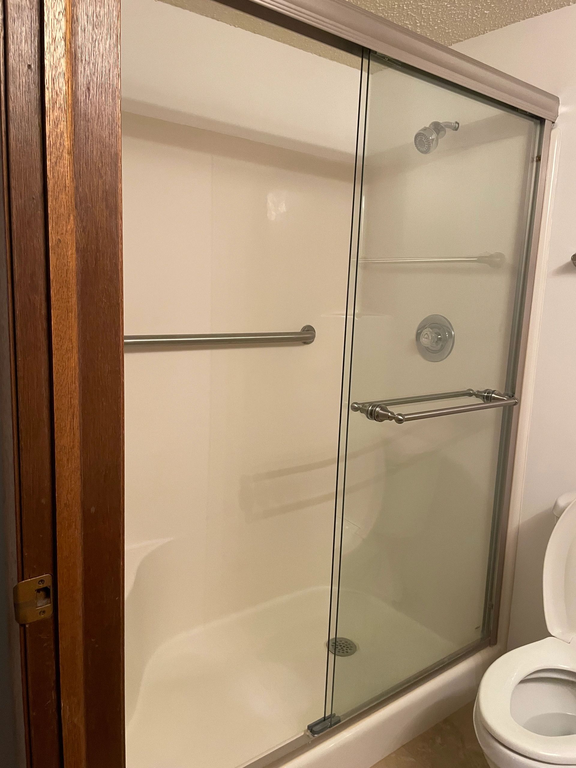 Clean bathroom shower with sliding glass doors and a toilet beside it.