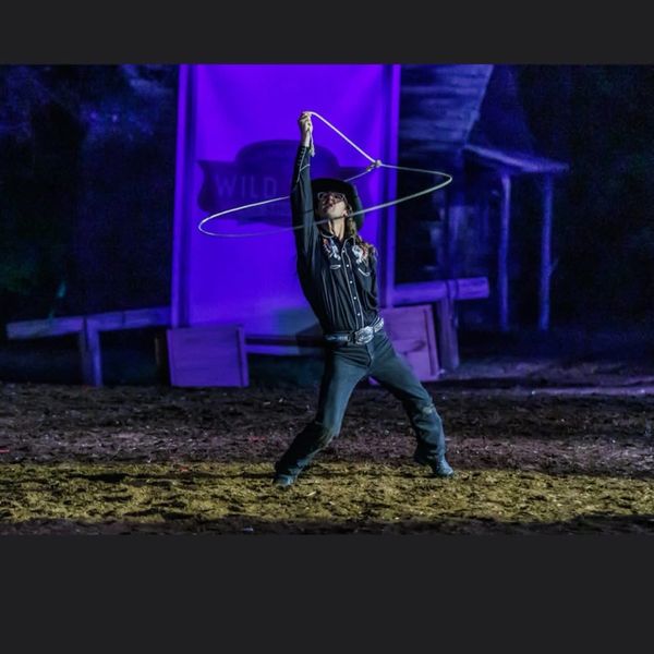 A cowboy performs a lasso trick under purple lighting.
