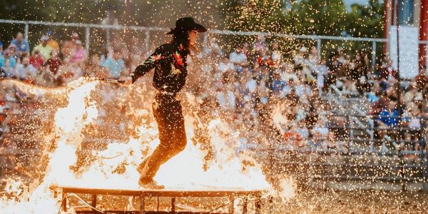 Performer in cowboy attire runs through fire during a public stunt show.