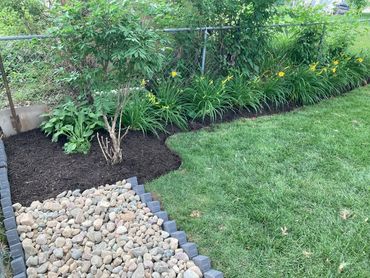 Garden bed with mulch, rocks, and green lawn.