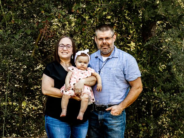 A happy family of three posing outdoors in casual attire.