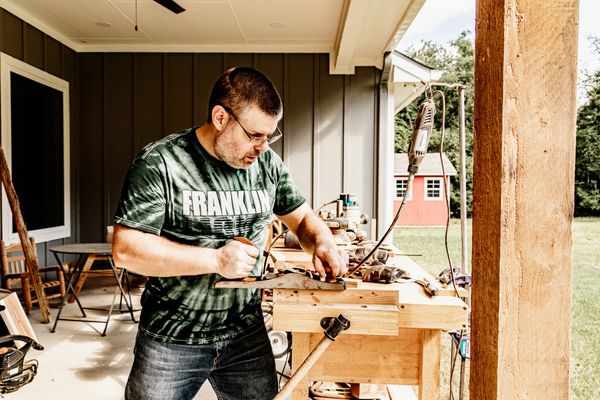 A man working with wood tools on a porch workbench.