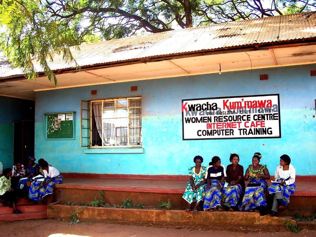 Women sitting outside a blue building with a women resource centre sign.
