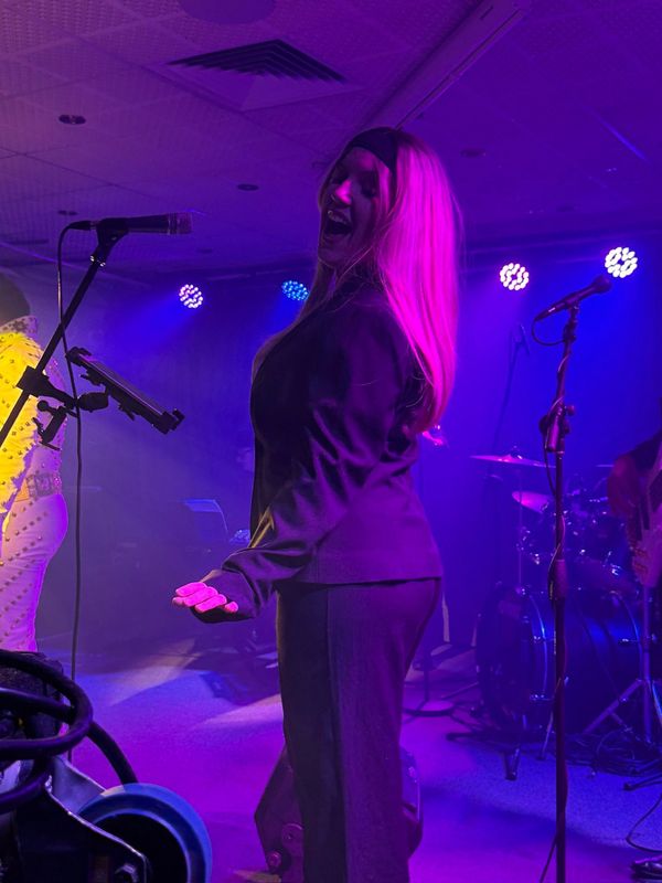 A female singer passionately performs under purple stage lights.