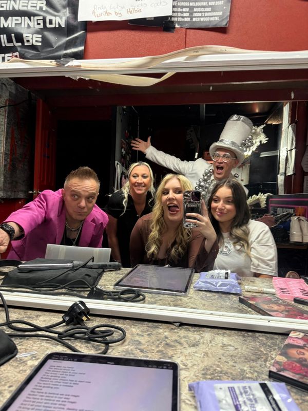 Group selfie in a lively dressing room with playful and excited expressions.