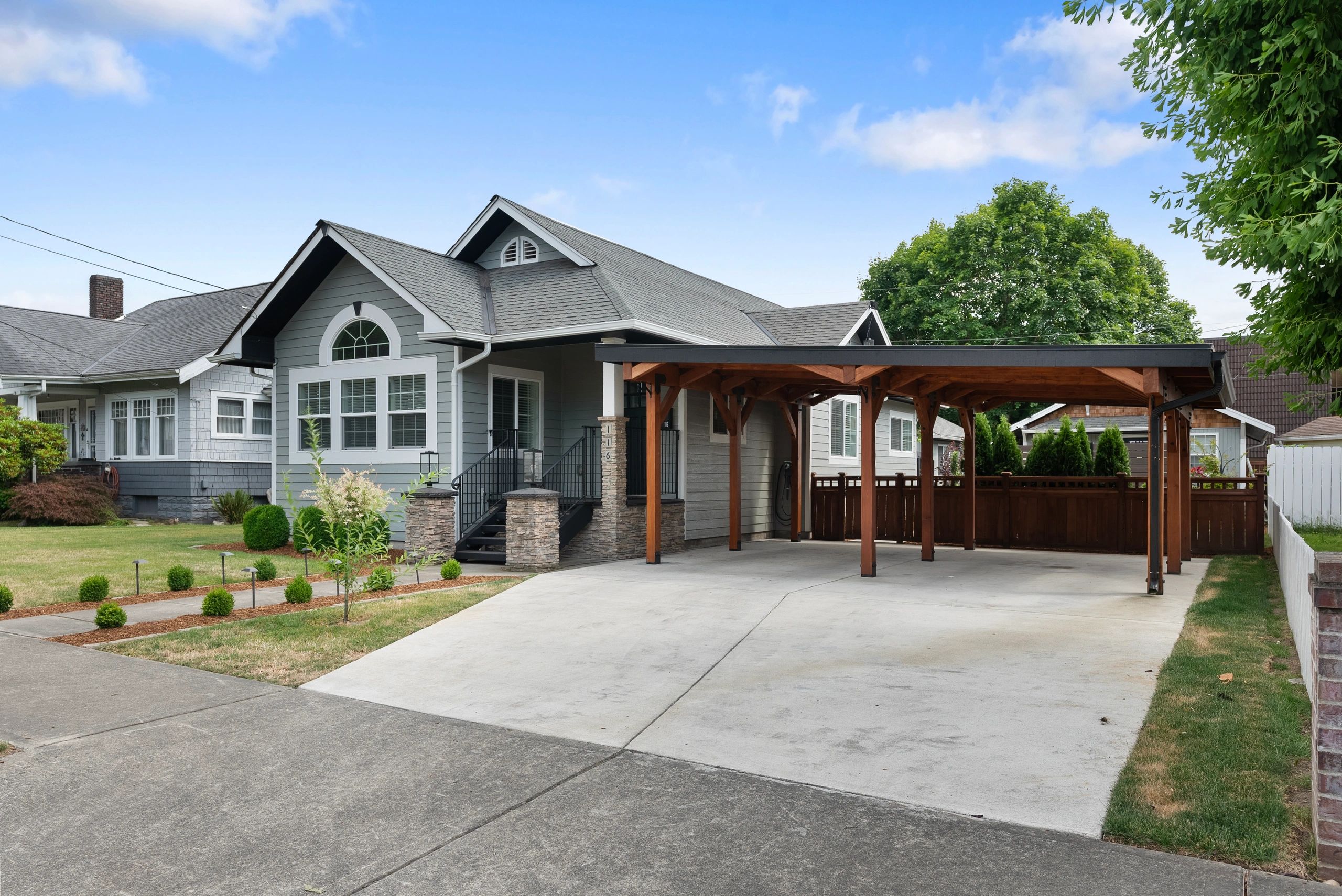 Charming gray house with a spacious driveway and wooden carport.
