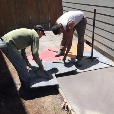 Two workers fitting colorful concrete stamps on a freshly poured patio.