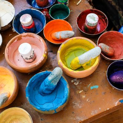Colorful powdered pigments in bowls with pestles ready for mixing.