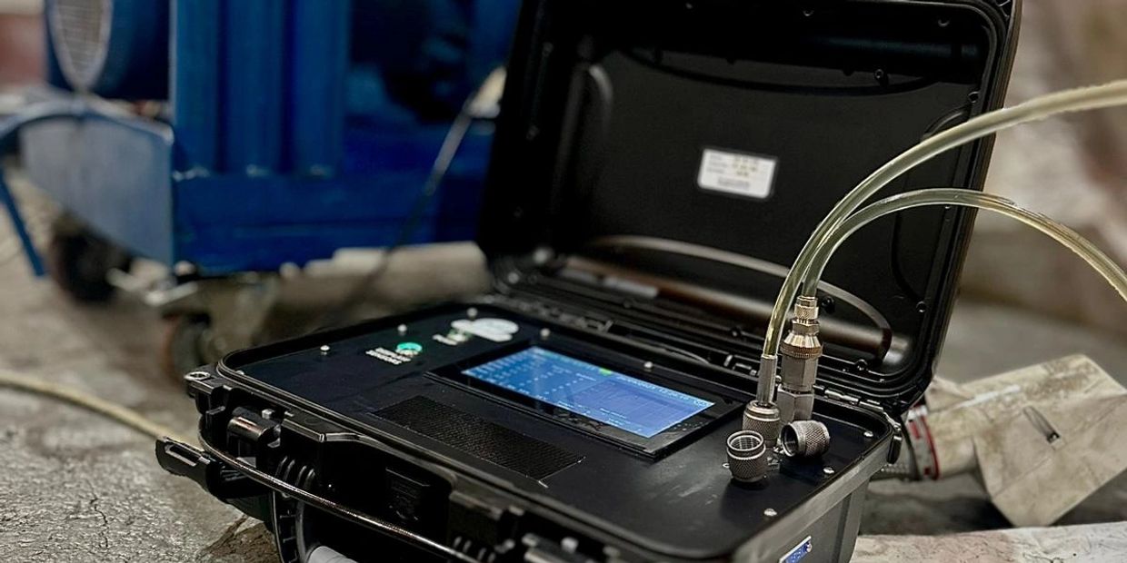 Portable diagnostic device connected with tubes beside industrial machinery.