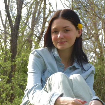 Young woman with a yellow flower in her hair sitting outdoors in nature.