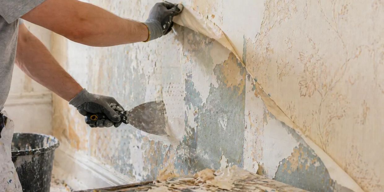 Person removing old wallpaper with a scraper tool.