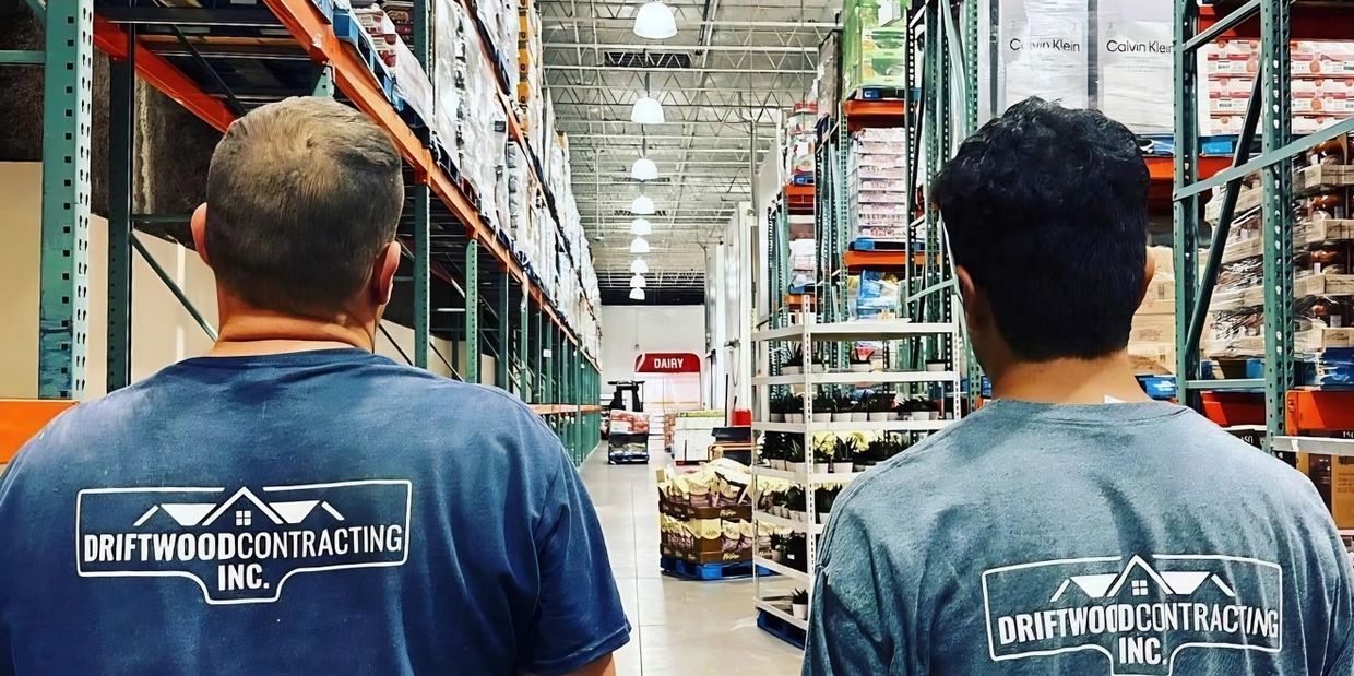 Two men in Driftwood Contracting shirts walk through a large warehouse aisle.