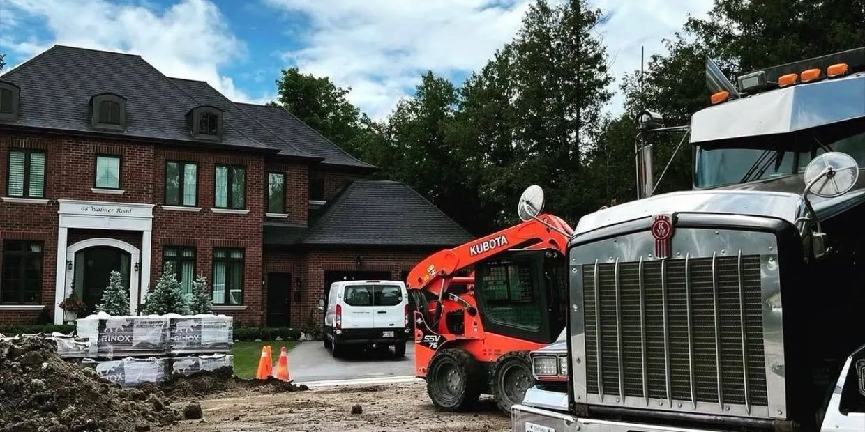 Active home renovation site with construction equipment, work trucks and a brick house.